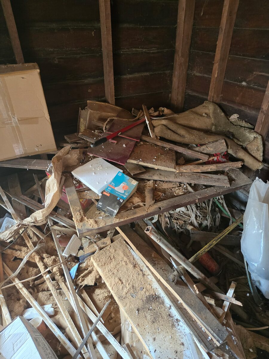 The inside of an old barn on a property cleanout, heaped with broken lumber, sacking and decades of stored belongings.